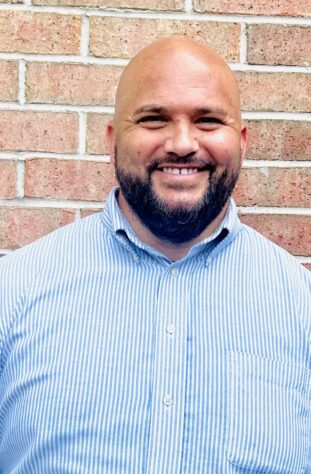 Smiling man in front of brick wall.